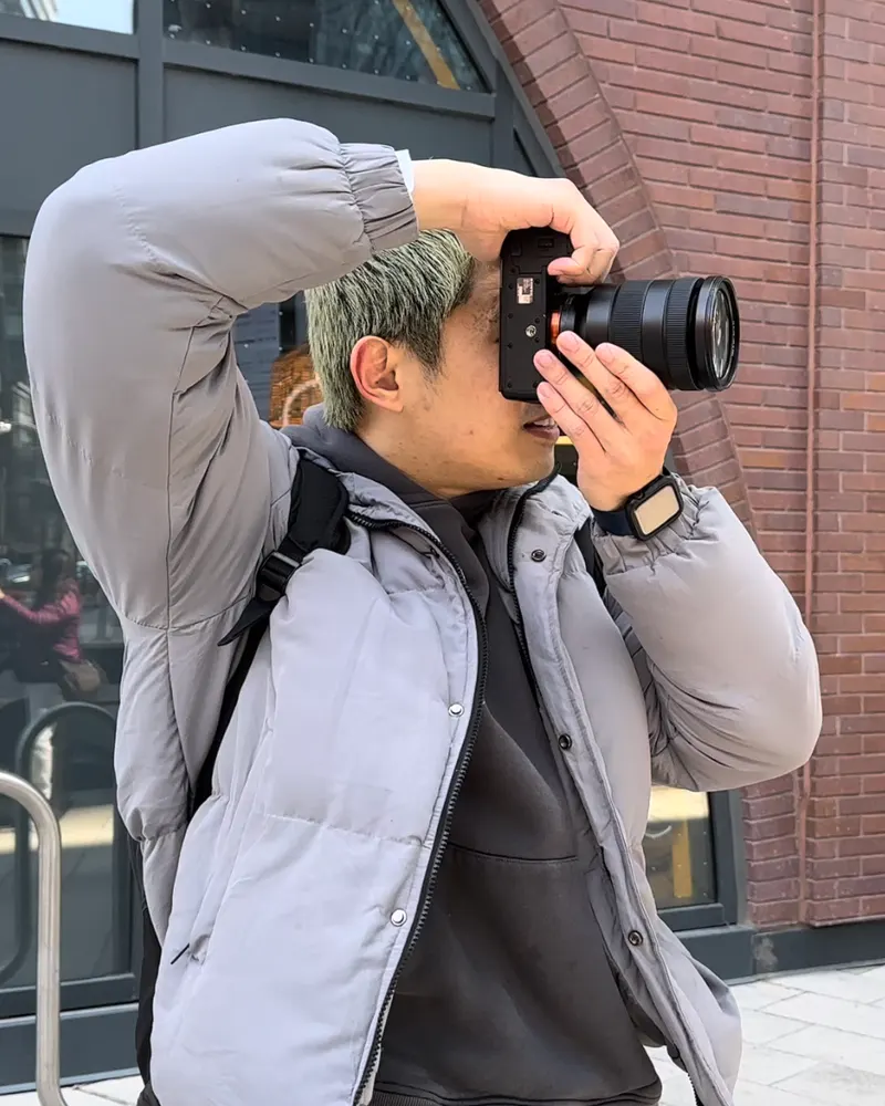 Aaron Lim shooting photos with a mirrorless camera outside a brick building