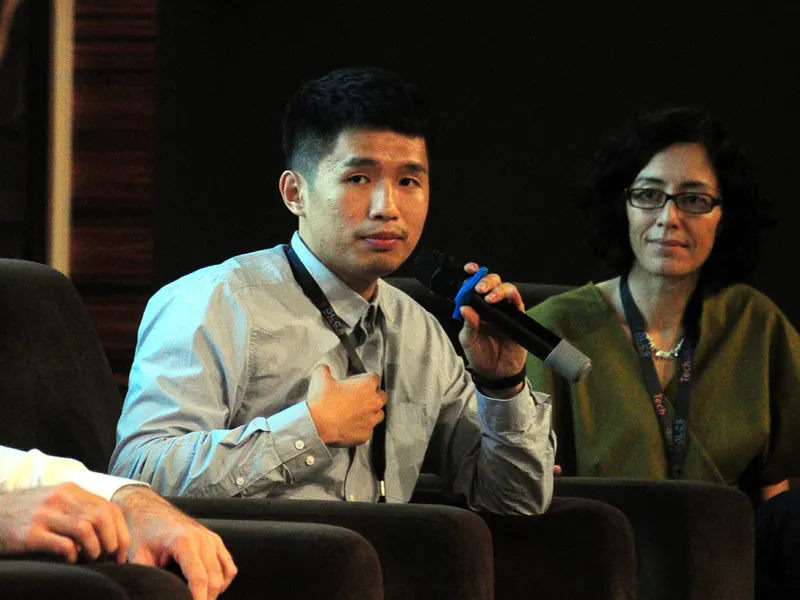 Aaron Lim answering a question on a panel, microphone in hand, 2017