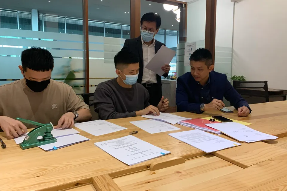 Aaron Lim and the deal team signing the Goody25 acquisition documents around a meeting room table, October 2020